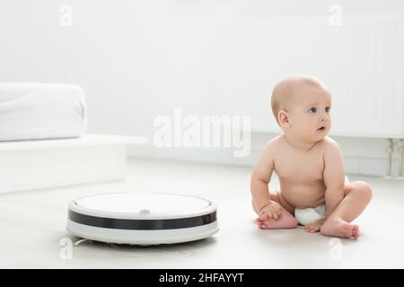 Little baby boy looks at the robotic vacuum cleaner at home. Stock Photo