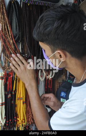 A young guy with wearing face mask choosing rosary beads in tibetan souvenir shop during coronavirus pandemic Stock Photo