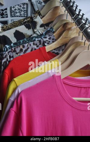 Multicolored t-shirts and shirts hanging on hangers in shop for sale - Stock Photo Stock Photo