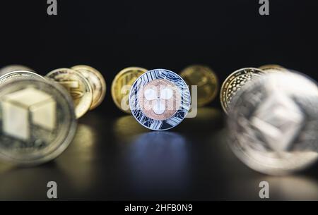 Ripple XRP next to many cryptocurrency coins like defocused Ethereum, Neo, Tether on black background. Central composition, low key photo for banners and news about crypto. Stock Photo