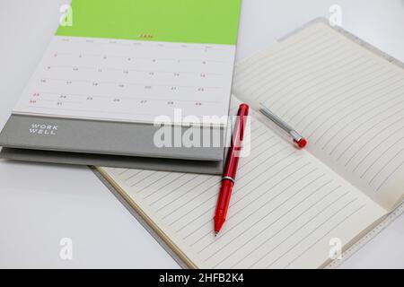 Blank Page of open Notebook with Red Pen and January 2022 Calendar on white desk Stock Photo