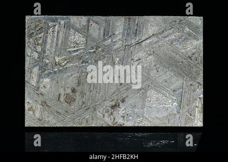 Acid-etched Muonionalusta meteorite plate with Widmanstetten patterns on a black background close up Stock Photo