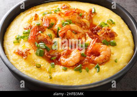 Homemade shrimp and grits with smoked bacon, onions and cheese in a black bowl on a dark concrete background. American cuisine. Horizontal Stock Photo
