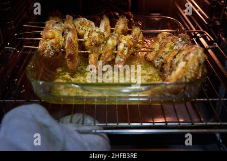 Hand with glove taking out of the oven a glass tray with chicken wings roasted in a healthy way Stock Photo