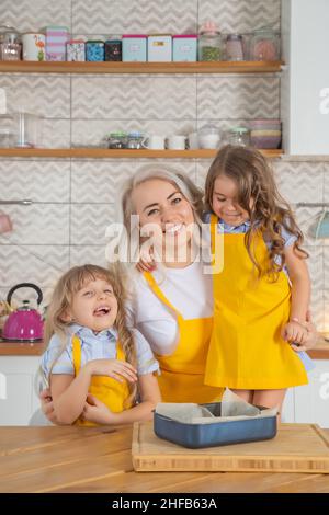Caucasian Mom and two daughters taste the cookies just cooked together in the kitchen. Home cooking concept Stock Photo