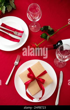 Romantic table setting for Valentines day. Fork and knife and gift box with red ribbon on the plate Stock Photo