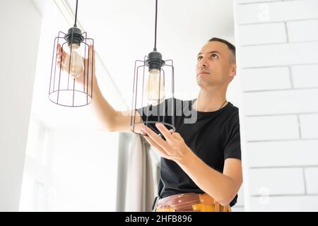 Worker repairing lamp on stretch ceiling indoors Stock Photo