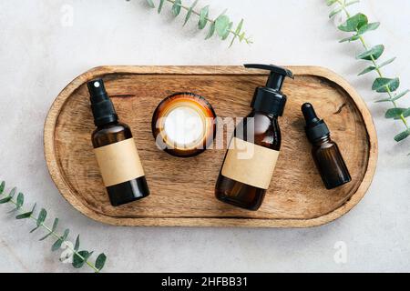 Top view set of SPA natural organic beauty products in amber glass containers on wooden plate with eucalyptus leaves. Stock Photo