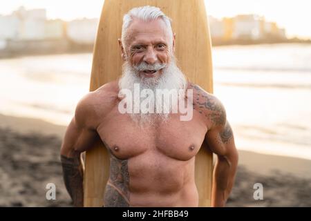 Fit senior man having fun surfing on tropical beach - Elderly healthy people lifestyle and extreme sport concept Stock Photo