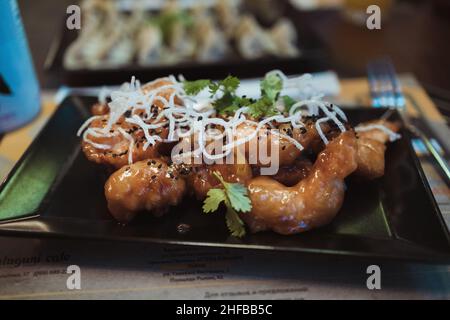 Shrimps tempura in batter in black plate on dark concrete surface at the restaurant. Closeup view Stock Photo