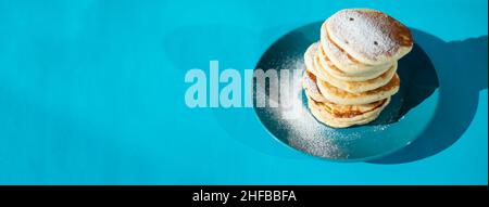 A stack of pancakes on a bright ceramic plate. Powdered sugar. Turquoise background. Stock Photo