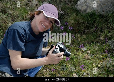 Smiling woman with camera photographing wild orchids in flower, Cavall Verd near Benimaurell, Alicante Province, Spain Stock Photo