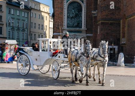 Cracow, Poland - 9th March 2020: Tourists enjoying a horse and carriage ride, an hour long tour around Krakow. White and black house with man outside Stock Photo