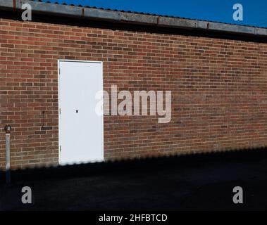 A stretch of brick wall with a white door, shadow, roof and blue sky. Stock Photo
