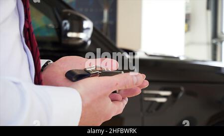 Woman hand with manicure, bracelet, and rings taking car keys from a man seller at the dealership. Salesman hand giving new car keys to a customer wom Stock Photo