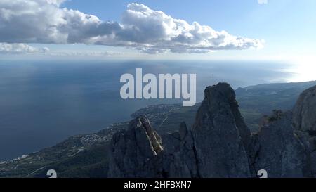 Aerial of steep mountains and funicular with people standing on the edge. Breathtaking seascape with rocks and blue cloudy sky on the background. Stock Photo