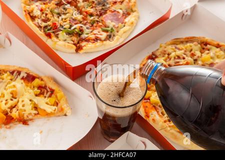 fast food served on the table, pizza with delicious ingredients and hands pouring soda in a glass cup, food and drinks in studio, restaurant Stock Photo