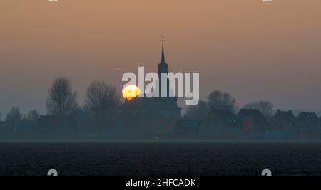 An orange sun sets behind the Church of St Nicholas in the village Wolphaartsdijk in the province Zeeland, The Netherlands Stock Photo