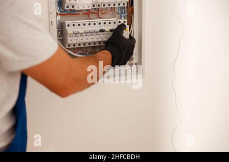 Hand of electrical technician checking fuses in a switchboard on the wall Stock Photo