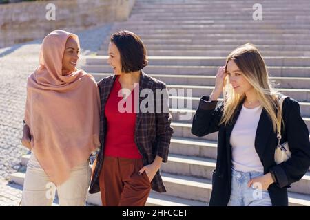 Positive young diverse female friends walking downstairs in campus Stock Photo