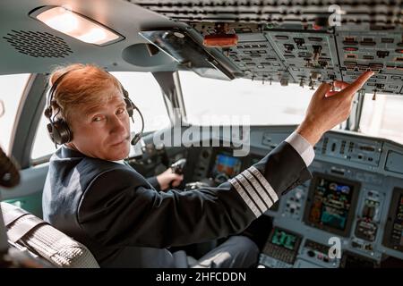 Male pilot pressing button on overhead panel in aircraft cockpit Stock Photo