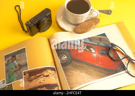 open family photograph album book. on a yellow table top, with a cup of coffee cookies a pair of reading glasses  and a point and shoot Sony camera Stock Photo
