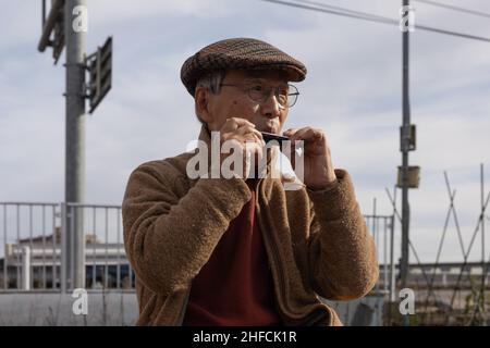 Senior citizen plays a harmonica during Dondo-Yaki in Aobadai.Dondo-Yaki is a traditional event usually held in mid-January and is considered the end of New Year celebrations in Japan. During this event Shimekazari (lucky charms) which were used to attract the Gods to people's homes are burned in a Shinto ceremony called Oharai. It is performed to keep bad luck away from people. After the fire stops soaring, Dango (mochi rice cake) or sweet potatoes are roasted above the bonfire. The origin of Dondo-Yaki can be traced back to the Heian period when nobles burnt bamboo in their palaces after the Stock Photo