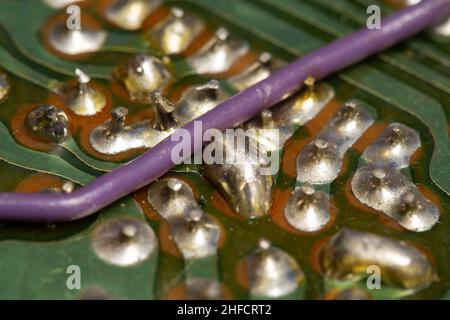 Purple wire over a green and old printed circuit board (PCB). Stock Photo