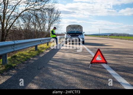 The red triangle warns of a broken down car stopped on the shoulder of the road Stock Photo