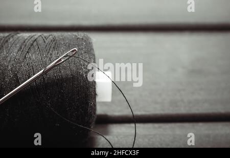 Needle with black thread. Spool of thread close up on wooden background Stock Photo