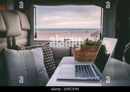 Remote onilne work and smart working travel concept with laptop computer inside a van camper interior with beach view. Freedom from office modern life Stock Photo