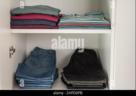 Neatly folded sweaters and jeans and other clothes on shelves in wardrobe Stock Photo