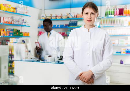 Experienced female pharmacist standing on background with male colleague in pharmacy Stock Photo