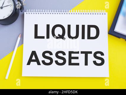 Conceptual hand writing showing Liquid Assets. Business photo text Cash and Bank Balances Market Liquidity Deferred Stock Open notebook squared page b Stock Photo
