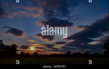 Beautiful sunset over a rural field, boasting a plethora of colours ranging from rich golds to deep indigo and purples, with stratocumulus clouds. Stock Photo