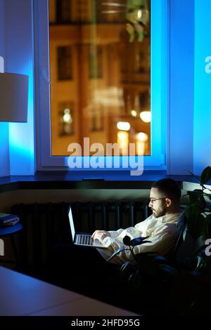 Tired programmer in dark office work on laptop. Workaholic businessman typing on computer at night Stock Photo