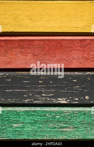 Background of multi colored rough boards, yellow, red, black, and green. Peeling paint wood texture with old faded colors. Rustic wooden pattern wall. Stock Photo