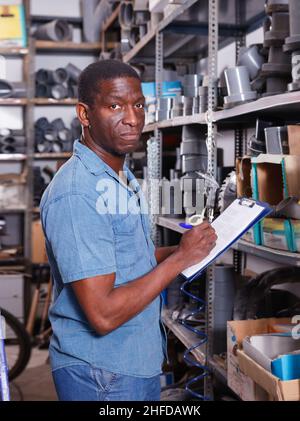 African American salesman checking goods availability on shelves of building materials shop Stock Photo