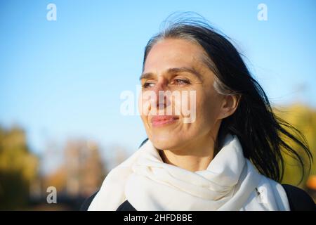 Profile side view portrait of attractive cheerful dreamy grey-haired middle-aged woman relaxing outdoors during sunny day Stock Photo