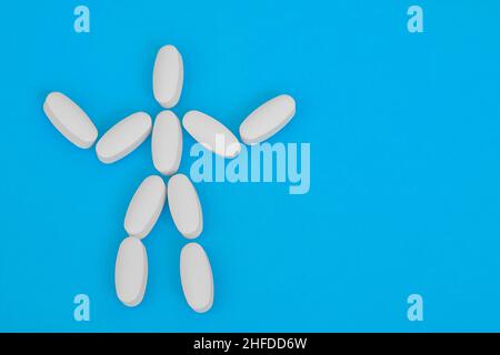 Human figure laid out from white oblong pills on blue background. Human skeleton. Medicine and treatment concept. Stock Photo