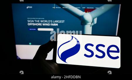 Person holding smartphone with logo of British energy company SSE plc on screen in front of website. Focus on phone display. Stock Photo