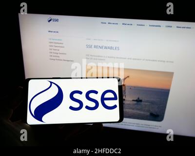 Person holding mobile phone with logo of British energy company SSE plc on screen in front of business web page. Focus on phone display. Stock Photo