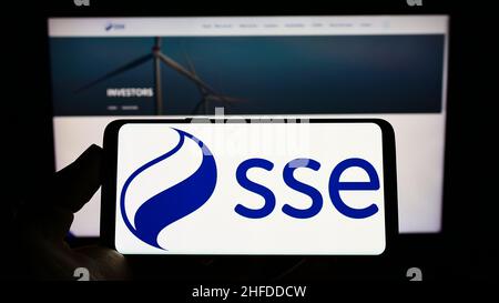 Person holding cellphone with logo of British energy company SSE plc on screen in front of business webpage. Focus on phone display. Stock Photo