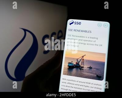 Person holding cellphone with webpage of British energy company SSE plc on screen in front of business logo. Focus on center of phone display. Stock Photo