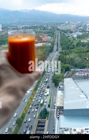 Hand holding carrot juice with the top view of avenue leading up to Almaty mountains, Kazakhstan Stock Photo