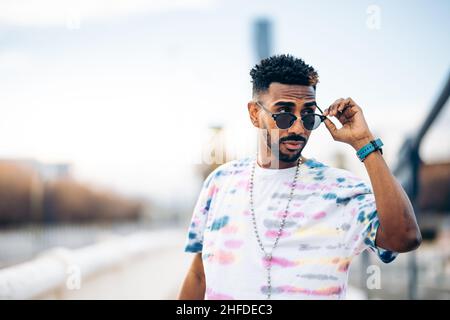 Portrait of a black man in colorful t-shirt looking over his sunglasses Stock Photo