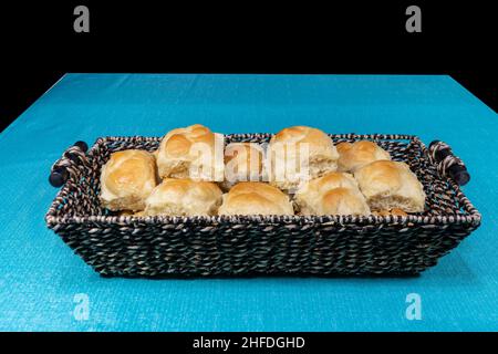 A basket of fresh baked, home cooked dinner rolls with fluffy texture and golden brown crust in a wicker basket on a table waiting to be served. Stock Photo
