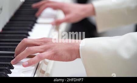 Close-up hands of a young man in a white jacket play music on the piano.Classical music, concert, performance.Music lessons on the piano, keyboard ins