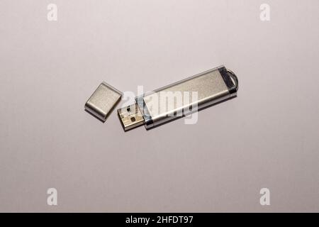 A silvery USB flash drive with an open cap, fairly used with a worn casing coating, lies on a white surface, selective focus Stock Photo