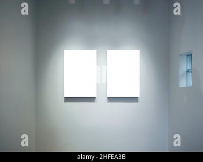 Two mockup vertical rectangle painting frames hanging on white wall background with spotlights. Blank white canvas frame with empty space in gallery, Stock Photo